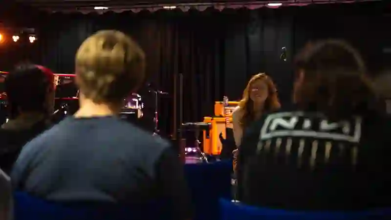 A workshop leader speaking with participants in a studio, instruments behind her