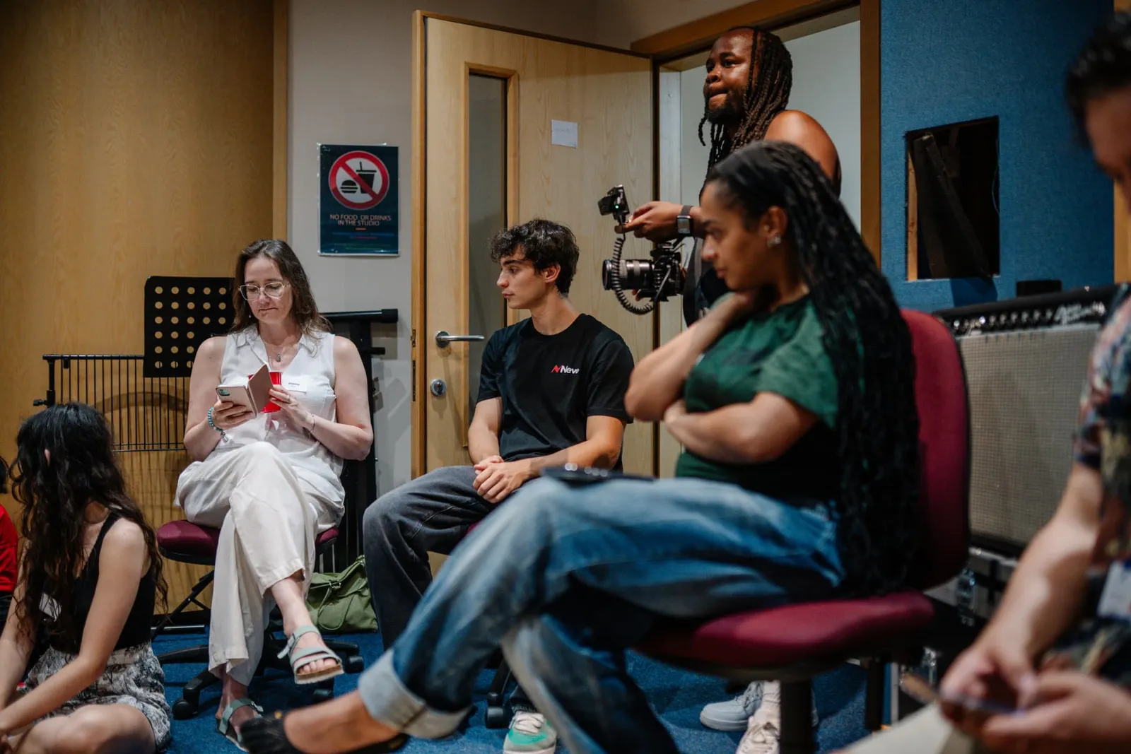 A group gathered in a music studio while a camera operator records.