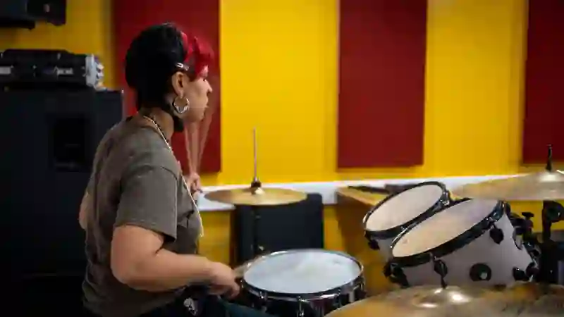 A young drummer playing in a studio with yellow and red wall panels