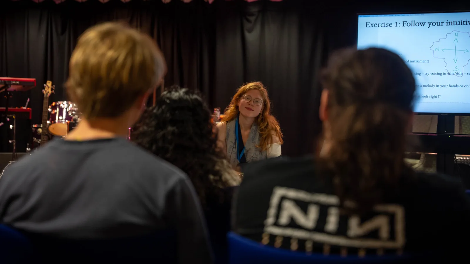 A young woman talking with a group of young musicians during a session